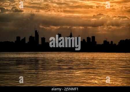 Skyline von Warschau bei Sonnenuntergang, goldenes Licht in Himmel und Fluss und Silhouette der Innenstadt der Hauptstadt Polens. Stockfoto