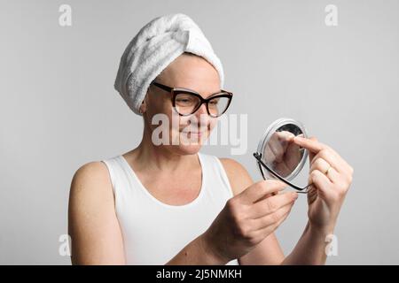 Kaukasische Frau mittleren Alters nach dem Bad sah in ihrem Spiegel Spiegelbild. Tägliche Routine der Gesichtsbehandlung Stockfoto