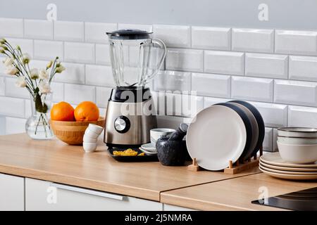 Bild von elektrischem Mixer, Satz von Keramikplatten und anderen Küchenwaren auf dem Tisch in der Küche Stockfoto