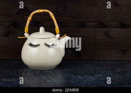 Weiße Teekannen mit Augen auf schwarzem Hintergrund. Lustige Gerichte mit falschen Wimpern. Stockfoto