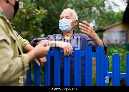 Die guten Nachbarn in der Schutzmaske reden über die Grenze ihrer Höfe Stockfoto