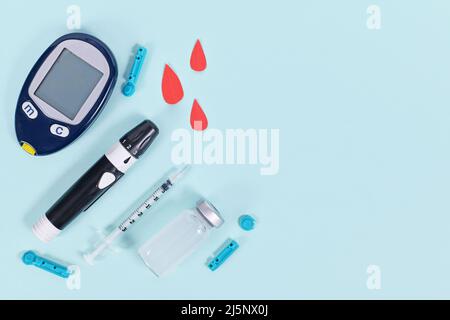 Geräte zur Behandlung von Diabetes mit Blutzucker-Messgerät, Lanzette, Insulinfläschchen und Spritze auf blauem Hintergrund Stockfoto