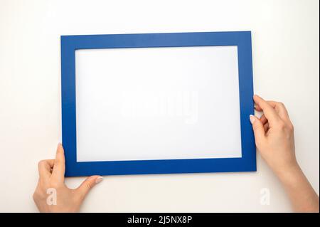 Bildmockup. Foto-Mockup mit Neigungswinkel. Frau Hände halten blauen Rahmen. Rahmengröße A4. Isoliert auf weißem Hintergrund. Leerer Fotorahmen mit CO Stockfoto