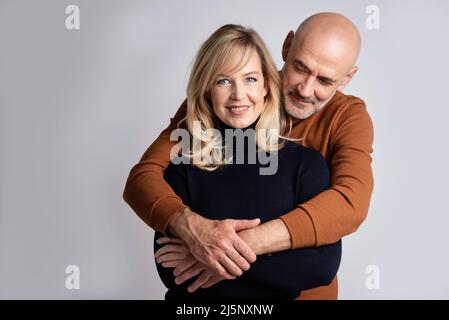 Studioaufnahme eines glücklichen Paares mittleren Alters, das auf einem isolierten Hintergrund mit Kopierfläche zusammensteht. Glückliche Mand versprödet schöne blonde haarige Frau Stockfoto