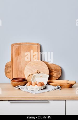 Bild eines Küchentischs mit Holzbrettern und frischen Hühnereiern im Korb gegen die blaue Wand Stockfoto