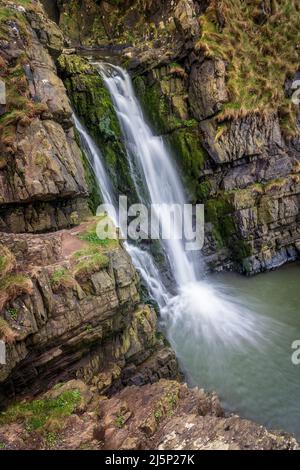 Der Wasserfall Speke's Mill Mouth liegt nur einen kurzen Spaziergang über die Klippen vom Hartland Quay entfernt. Die Wasserfälle stürzen 48 Meter von oben auf den Strand unten in t Stockfoto