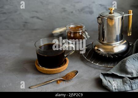 Frisch gebrühter Kaffee in Tasse und Kaffeekannen mit Rohrzucker auf grauem Hintergrund Stockfoto