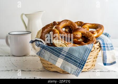 Brezeln oder Brezeln im Brotkorb mit Serviette mit Milchglas und Tasse Stockfoto