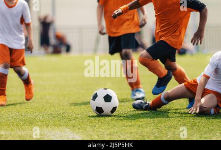 Gruppe von multiethnischen Kindern, die Fußballspiel spielen. Junge Jungs laufen nach dem Fußball auf dem Rasen Fußballplatz. Kinder in orange-weißem Jersey shir Stockfoto