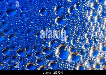Wasser tropft auf eine blaue Glasoberfläche Stockfoto