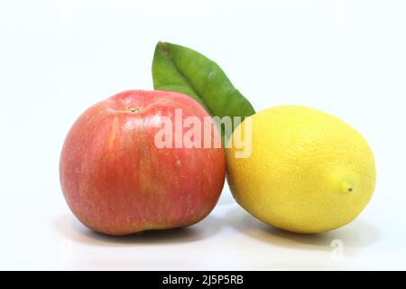 Eine Zitrone und ein Apfel auf weißem Hintergrund. Roter Apfel und gelbe Zitrone mit grünem Blatt auf weißem Hintergrund in natürlichem Licht Stockfoto