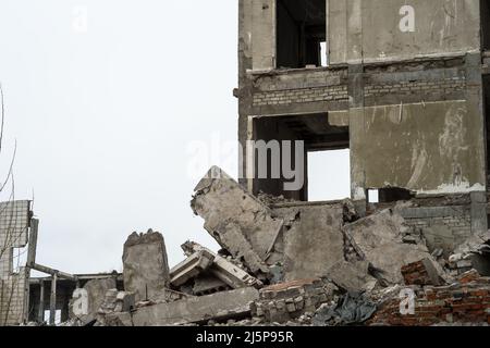 Ein zerstörtes Gebäude in Nahaufnahme vor einem grauen Himmel mit einem Haufen von Betonschutt, Platten und Pfählen im Vordergrund. Hintergrund. Stockfoto