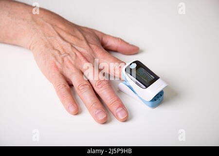 Mann mittleren Alters, der die Sauerstoffsättigung des Blutes mit einem digitalen Oximeter zu Hause misst. Stockfoto