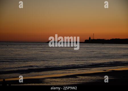 Farbenprächtiger Himmel bei Sonnenuntergang an der Küste von Conil in Spanien, mit Blick auf den Leuchtturm an der felsigen Küste Stockfoto