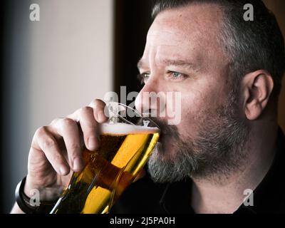 Nahaufnahme eines Hipster-Mannes in seinen 40s Jahren, der ein Glas Bier in einer Bar oder Kneipe trinkt. Stockfoto