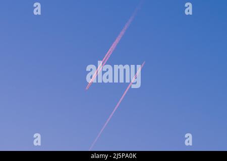 Blick auf zwei Passagierflugzeuge, die in der rot leuchtenden Abendsonne und am blauen Himmel parallel in entgegengesetzter Richtung fliegen Stockfoto