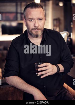 Porträt eines hübschen reifen Mannes, der ein Glas ordentlichen Whiskys in der Bar oder im Pub hält. Stockfoto