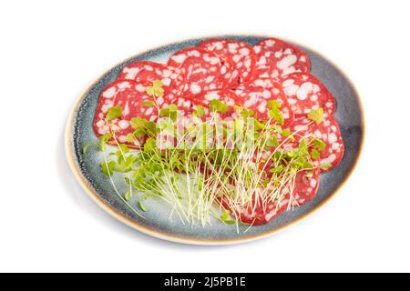 Scheiben geräucherter Cervelat-Salami-Wurst mit Spinat-Microgreen isoliert auf weißem Hintergrund. Seitenansicht, Nahaufnahme. Stockfoto