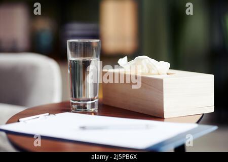 Glas frisches Wasser, leeres Blatt auf der Zwischenablage und Servietten für den Kunden auf dem Tisch im Büro des Therapeuten Stockfoto