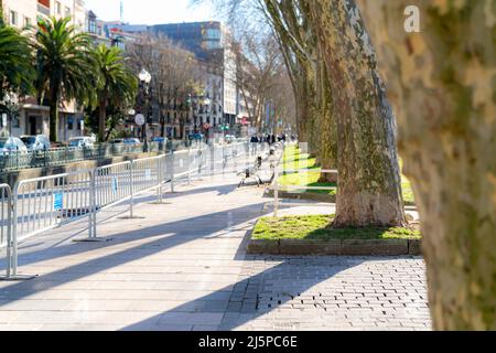 Bürgersteig am Morgen mit Sonnenlicht und großem Baum. Bürgersteig mit verwackelte Bank und Menschen tragen Schutzmaske beim Gehen auf dem Bürgersteig. Grüne Stadt. Verschwommen Stockfoto