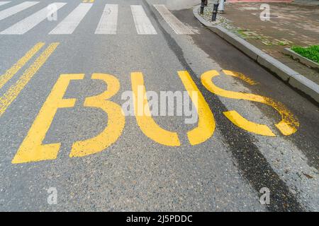 Word Bus ist gelb auf dem Asphalt geschrieben im Hintergrund ist eine Fußgängerüberfahrt. Stockfoto