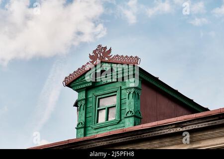 Fassade des Dachfensters auf dem Dach eines typischen russischen Landhauses mit geschnitzten Holzdekorationen Stockfoto
