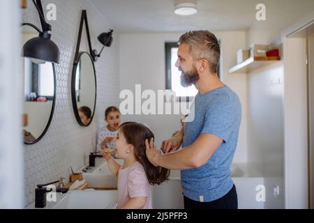 Vater putzt sich die Haare seiner kleinen Tochter im Badezimmer, morgendliches Routinekonzept. Stockfoto