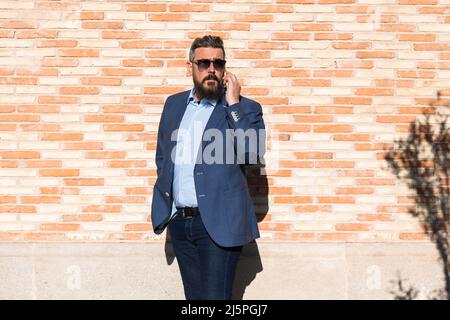 Ein erwachsener Mann, der gegen eine Ziegelsteinmauer steht und mit dem Mobiltelefon spricht Stockfoto