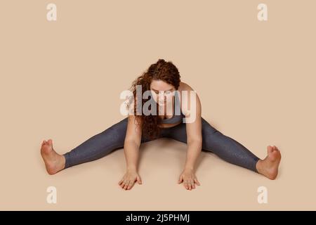 Nachdenkliche Augennachbarn übergroße Adipositas Frau mit überflüssigem Gewicht, dabei Stretching Hände auf dem Boden, gespaltene Beine Stockfoto