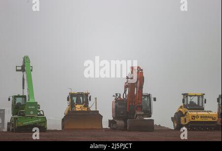 Meerane, Deutschland. 25. April 2022. Baufahrzeuge stehen auf einer Baustelle für eine neue Industriehalle. Die Grundsteinlegung für die Halle 7 im Industriepark Meerane am selben Tag stellt die weitreichende Fertigstellung des Industrieparks dar. In der Logistikhalle soll die Achsmontage ausgebaut werden, die fast in Sichtweite des VW-Moselwerks in Zwickau auf der gegenüberliegenden Straßenseite stattfindet. Hier werden die Achsen für die Elektrofahrzeuge des VW-Konzerns gefertigt. Quelle: Jan Woitas/dpa/Alamy Live News Stockfoto