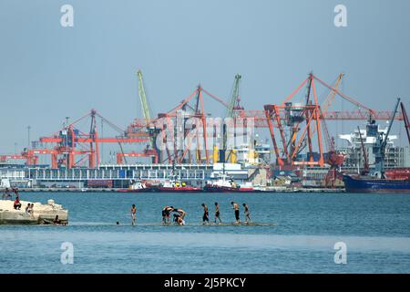 Türkische Jungen spielen an einem heißen Sommertag im türkischen Mersin auf einer Betonplattform im Mittelmeer. Im Hintergrund ist der Hafen von Mersin. Stockfoto