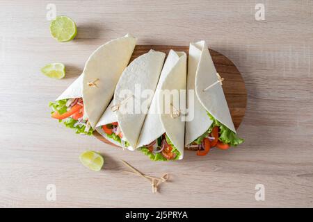Draufsicht auf vier verpackte Buritto mit Gemüse und Hühnerfilet auf einem Holzbrett und Küchentisch. Hausgemachte Speisen Stockfoto