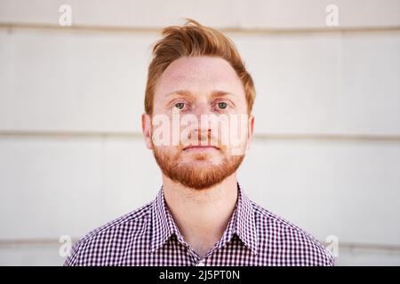 Outdoor-Porträt eines roten Haares, der die Kamera ernst mit heiterem Gesicht ansieht. Nahaufnahme eines konzentrierten Mannes - kaukasischer junger Mann. Menschen und Stockfoto