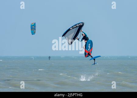 Ein Wing Surfer auf einem Tragflächenboot, das im Winter im Golf von Mexiko auf South Padre Island, Texas, aus dem Wasser springt. Dahinter ist ein Kite-Surfer. Stockfoto