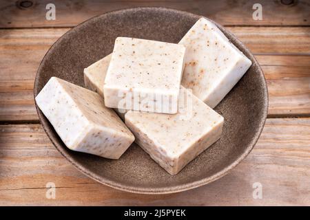 Handgemachte Seife mit getrockneten Lavendelblüten in brauner Schale auf Holzgrund. Stockfoto