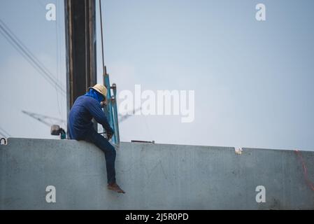 Rückansicht eines asiatischen Arbeiters, der am Rand eines Gebäudes auf der Baustelle arbeitet. Stockfoto