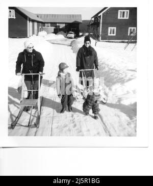 60iger Jahre authentisches Vintage-Foto von zwei Müttern mit kleinen Kindern, die Schlitten durch den Schnee schieben, Schweden Stockfoto