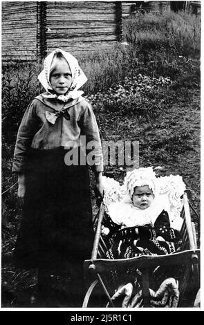 Das authentische Vintage-Foto aus dem Jahr 1910 zeigt das Kind im Stehen und das Baby im Holzkarren im Freien, bei der Kamera, Schweden, Skandinavien Stockfoto