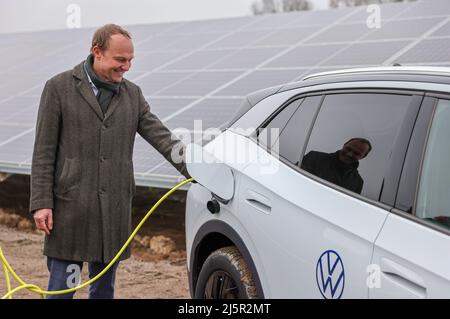 25. April 2022, Sachsen, Zwickau: Wolfram Günther (die Grünen), Sachsens Energie- und Klimaschutzminister, steckt den Ladestecker in einen VW ID.4 in einem neuen Solarpark. Die Enerparc AG betreibt den sechs Hektar großen Solarpark Mosel und wird in den nächsten 20 Jahren jährlich 5,5 Millionen kWh Solarenergie für die Produktion der vollelektrischen Volkswagen-Modelle aus Zwickau liefern. Alle drei Volkswagen-Standorte in Sachsen werden bereits seit Ende 2017 mit Ökostrom aus Wasserkraft versorgt. Bisher kam dies jedoch aus Österreich. Zwickau ist nun der erste sächsische Standort, der erhalten hat Stockfoto