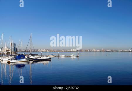 Jachten an den Anlegestellen, Cardiff Bay mit Millennium Center und Staudamm am Horizont. April 2022. Feder. Stockfoto