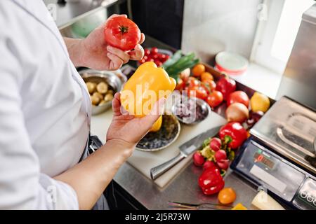Nahaufnahme eines professionellen Kochs, der frisches Gemüse für den Salat am Küchentisch auswählt Stockfoto
