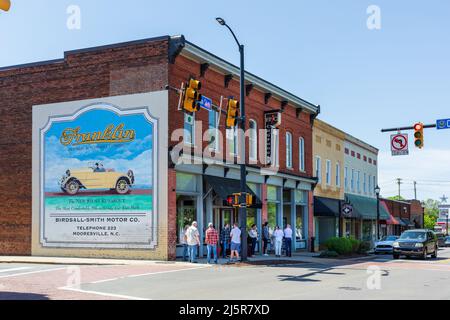 MOORESVILLE, NC, USA-17 APRIL 2022: Eine Gruppe von Menschen versammelten sich auf dem Bürgersteig vor dem Epic Chophouse an der Main Street. Historische Auto-Werbung. Stockfoto