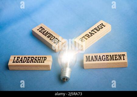 Business Concept Text auf Holzblöcken - Führung, Teamarbeit, Strategie und Management. Mit leuchtender Glühbirne. Stockfoto