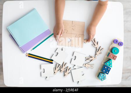 Draufsicht des Kindes mit hölzernen Puzzleteilen, kleine Hände, die Puzzles auf dem Tisch im Klassenzimmer verbinden, freier Platz Stockfoto