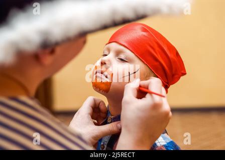 Animator macht Piratenmalerei auf Gesicht des Kleinkindes auf Kindergeburtstag. Niedlicher Junge in roten Bandanna bereitet sich für die Feier aus nächster Nähe Stockfoto