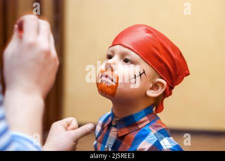 Animator macht Piratenmalerei auf Gesicht des Kleinkindes auf Kindergeburtstag. Niedlicher Junge in roten Bandanna bereitet sich für die Feier aus nächster Nähe Stockfoto