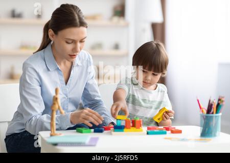 Nette kleine Junge Vorschulkinder spielen Entwicklung Holzspiele mit professionellen Frau Psychologin im Kindergarten Stockfoto