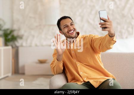 Lächelnder junger Mann, der mit dem Mobiltelefon die Hand schwenkt Stockfoto