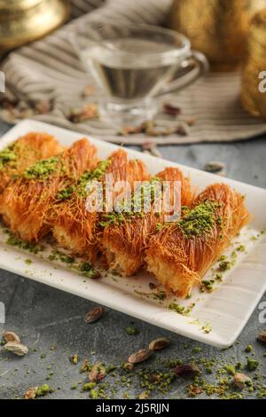 Hausgemachte arabische traditionelle Süßigkeiten Kunafa oder Konafa Rolle mit Käse oder Rahm und Zuckersirup Pistazie auf der Oberseite Stockfoto