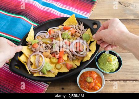 Hände, die Nahrung aus einem Tablett Nachos mit Fleisch nehmen. Schüsseln mit Salsa. Speicherplatz kopieren. Mexikanisches Küchenkonzept. Stockfoto